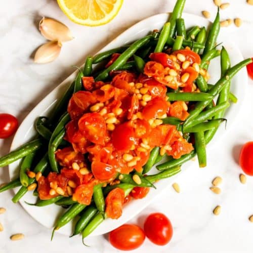 Platter of green beans topped with tomatoes and pine nuts