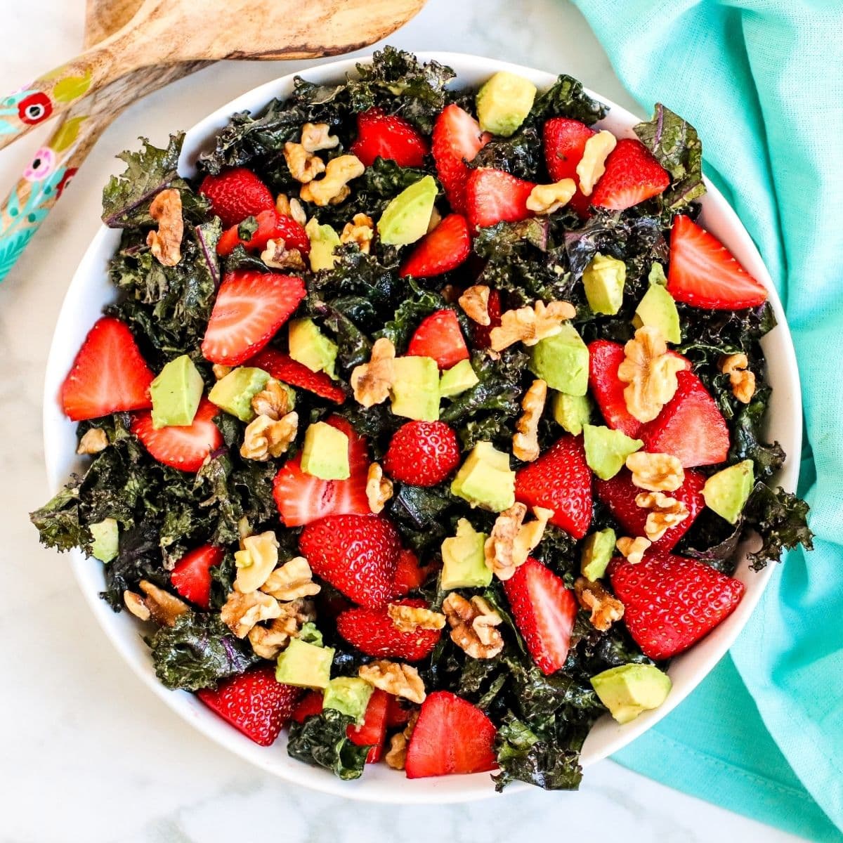 Overhead of serving bowl of kale salad topped with sliced strawberries, avocado cubes, and walnuts