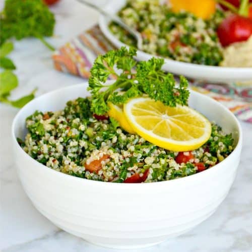 Bowl of quinoa tabbouleh salad garnished with sprig of parsley and slices or lemon