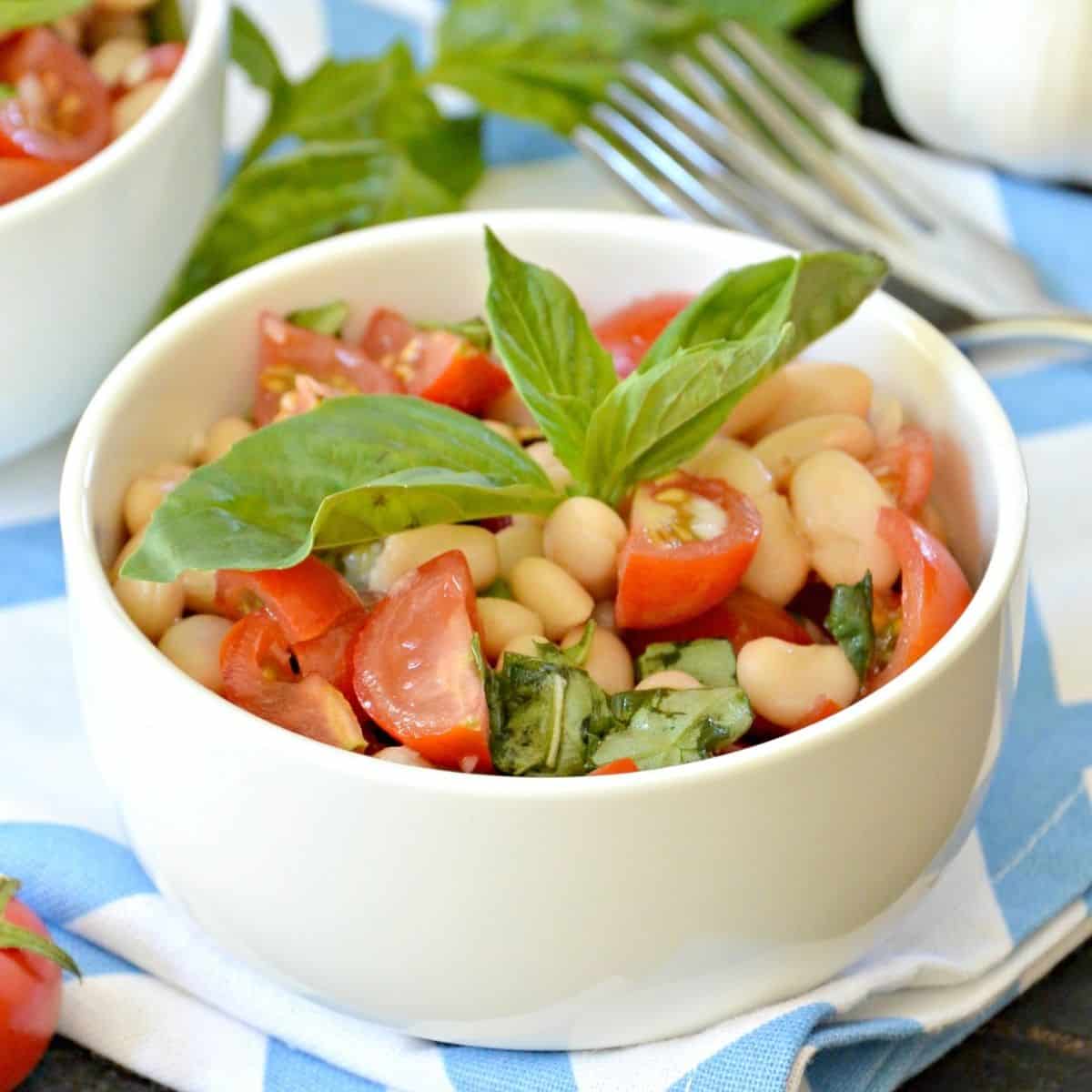 Bowl of bean and tomato salad garnished with sprig of fresh basil