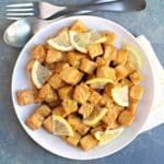 Plate of air fried tofu coated with lemon sauce and garnished with fresh lemon