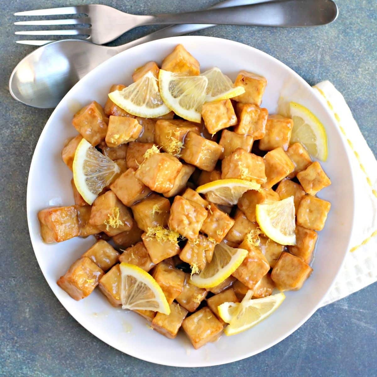 Plate of air fried tofu coated with lemon sauce and garnished with fresh lemon