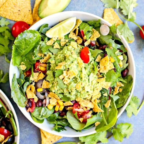 Bowl of salad topped with guacamole and crushed tortilla chips