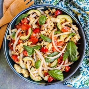 Bowl of salad with corn, tomatoes, cucumber, onions, and fresh basil