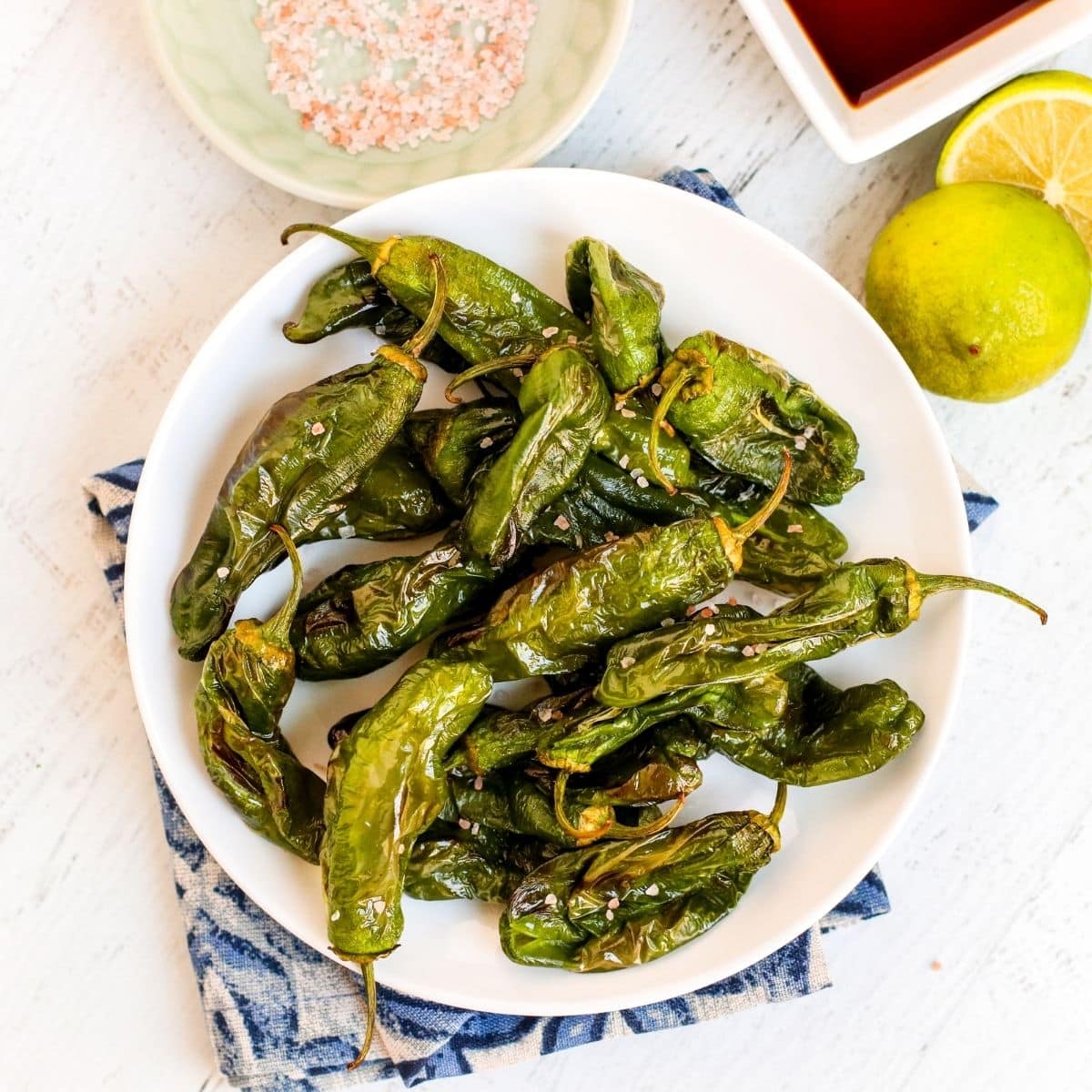 Plate of blistered Shishito peppers with pink salt, soy sauce, and lemon on the side