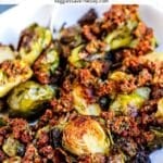 Bowl of roasted Brussels sprouts topped with vegan sun-dried tomato pesto with text overlay: Brussels Sprouts with Sun-Dried Tomatoes.