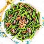 Serving bowl of green beans and mushrooms with gold utensils