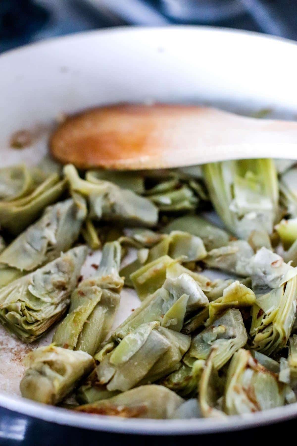 Sauteing artichoke hearts in a skillet.