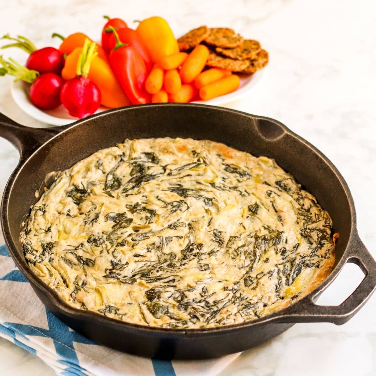 Cast iron skillet with baked dip and platter of vegetables and crackers in the background