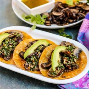 Platter of mushroom tacos topped with sliced avocado and chimichurri sauce.