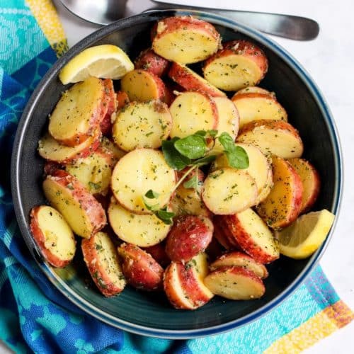 Bowl of Greek potato salad garnished with a sprig of fresh oregano