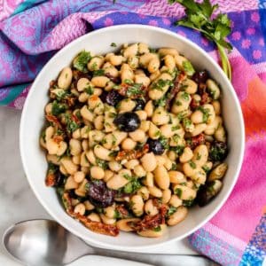 Bowl of white bean salad with olives and sun-dried tomatoes