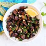 Bowl of roasted mushrooms garnished with pine nuts, parsley, and a lemon wedge