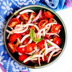 Bowl of tomato and onion salad garnished with a sprig of fresh basil