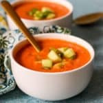 Bowls of cold tomato soup garnished with cucumber and green bell pepper