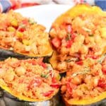 Four stuffed acorn squash halves on a plate with text overlay: Quinoa Chickpea Stuffed Acorn Squash.