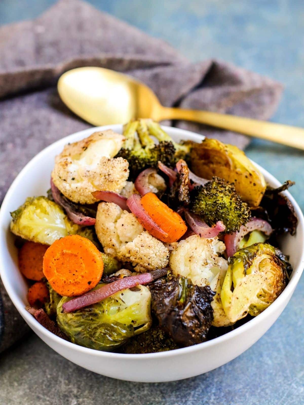 Bowl of roasted Brussels sprouts, carrots, cauliflower, broccoli, and red onions.