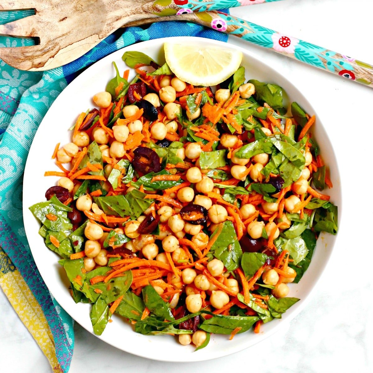 Serving bowl of spinach salad with chickpeas, carrots, and Kalamata olives.