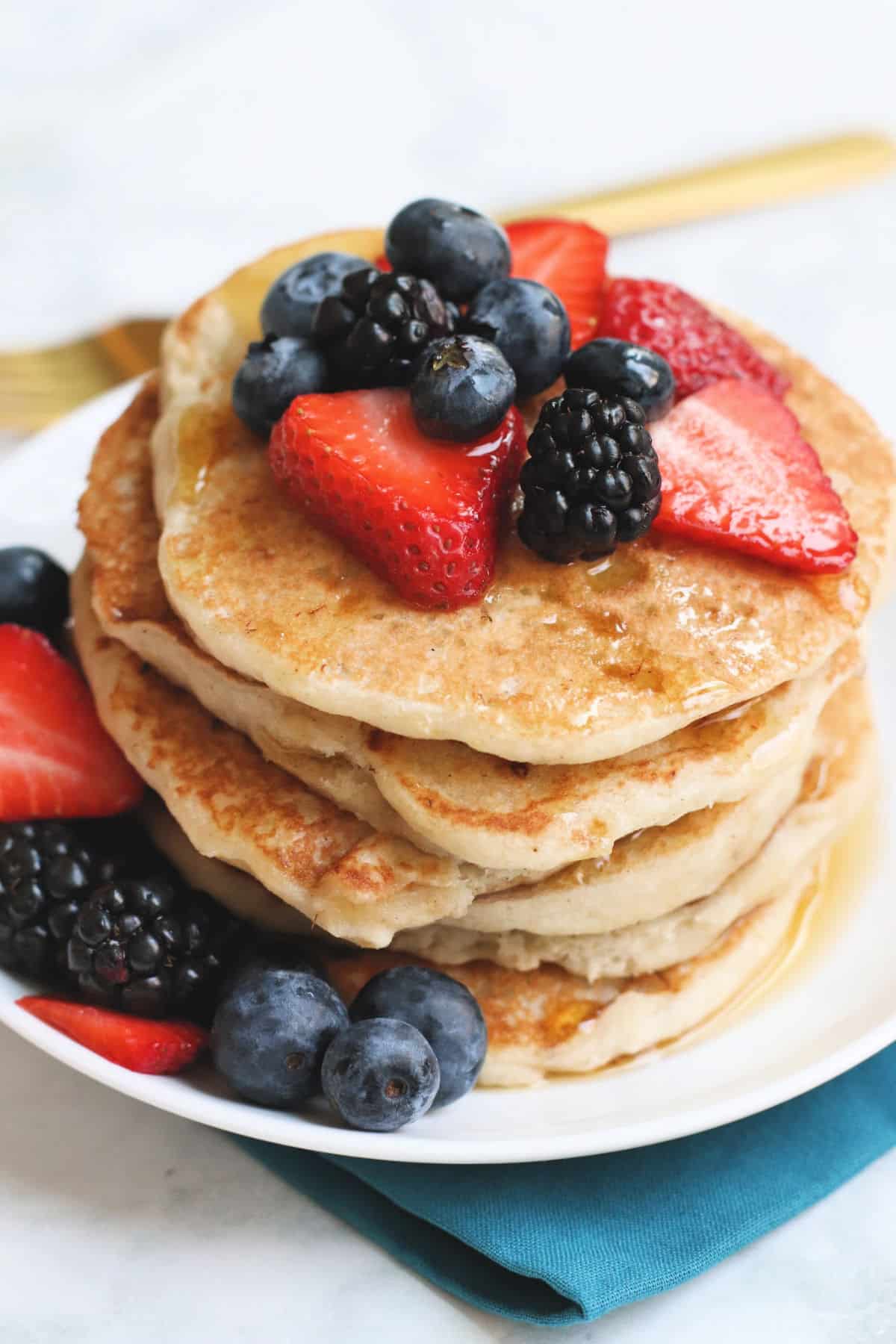 Stack of Easy Vegan Pancakes topped with fresh berries and maple syrup