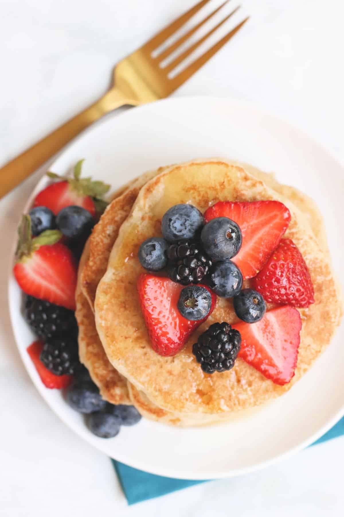 Overhead of plate of pancakes topped with blueberries, strawberries, and blackberries