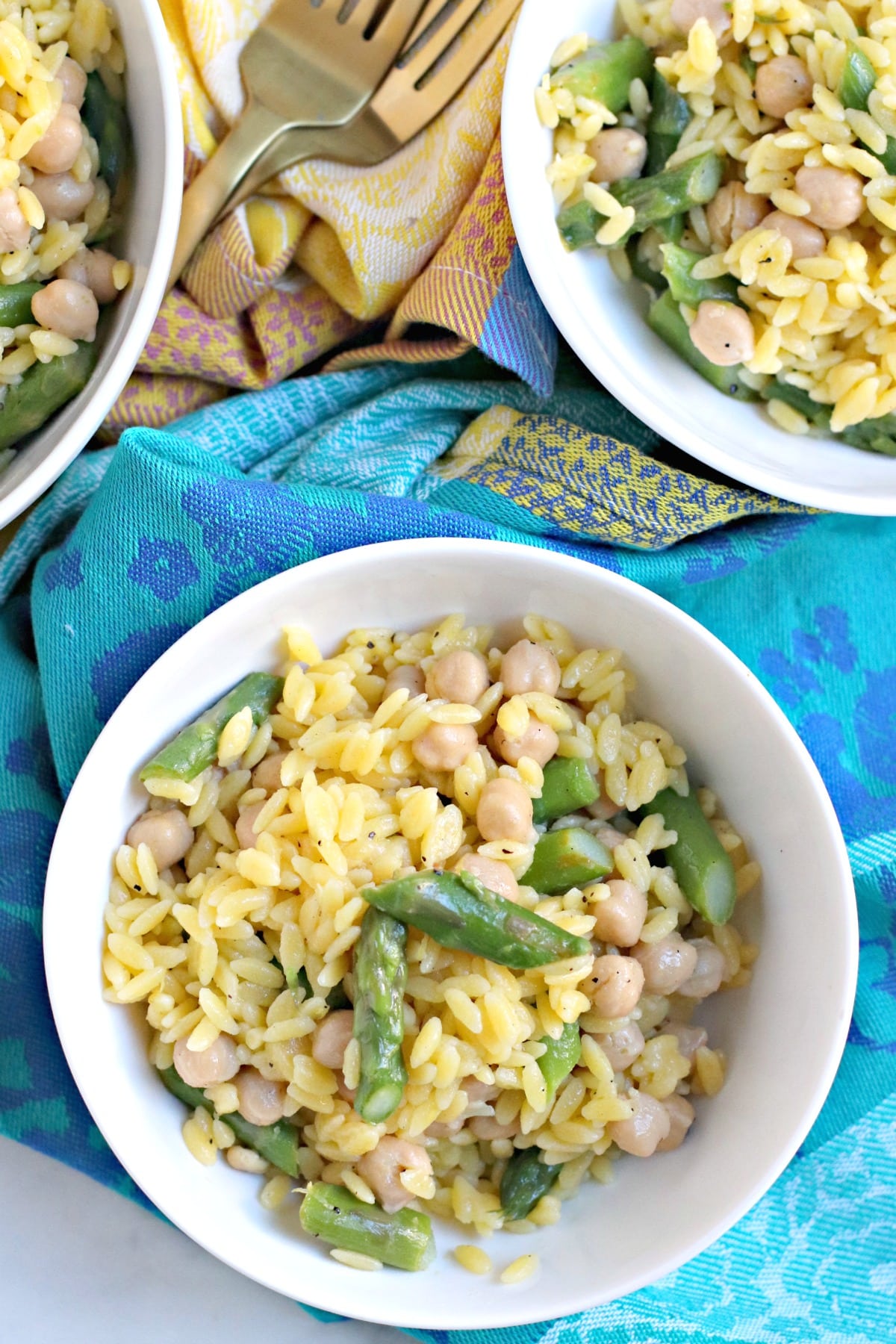 Overhead of white bowl of lemon orzo on a blue and aqua napkin.