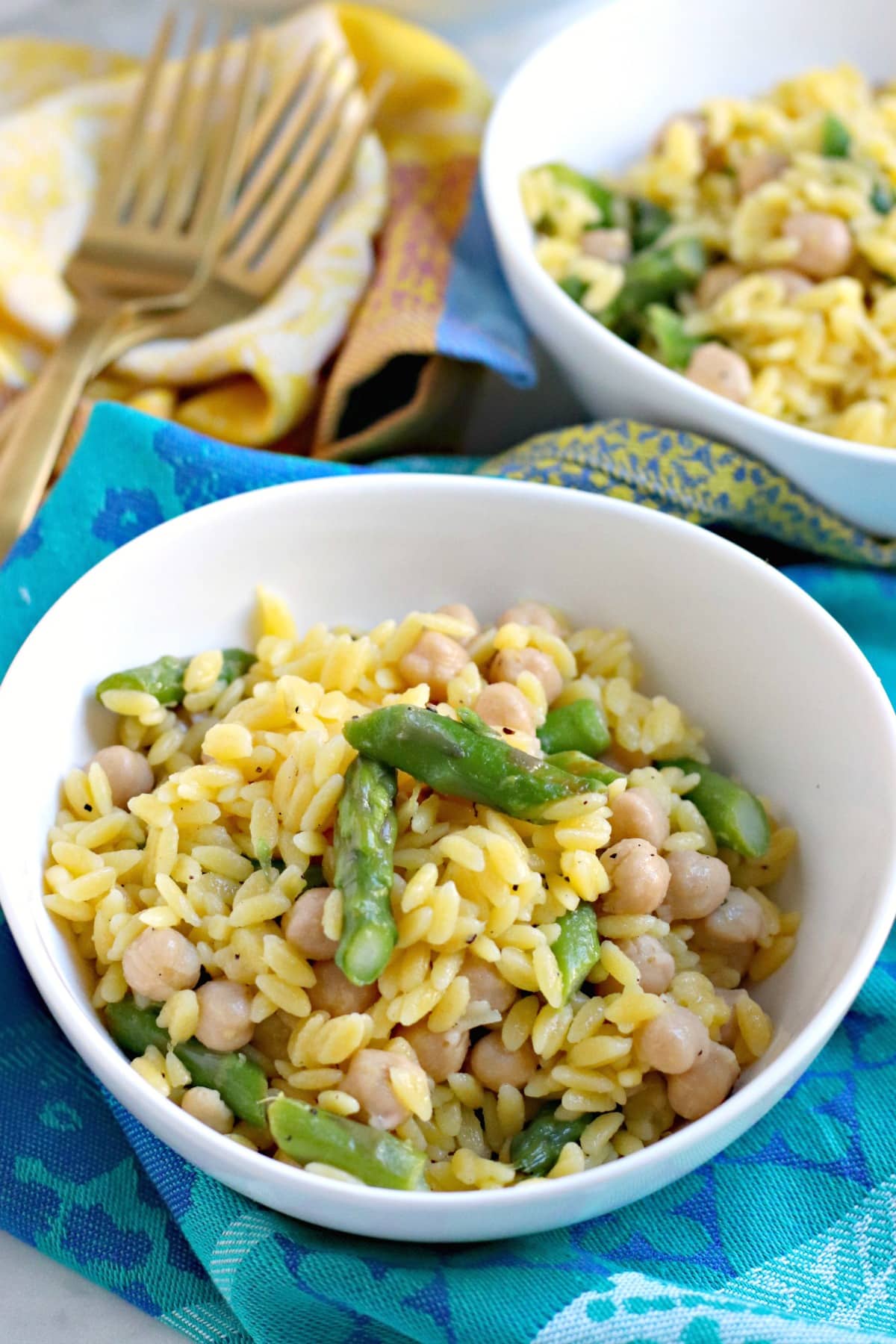 Close up of bowl of Lemon Orzo with serving bowl and gold forks in the background.