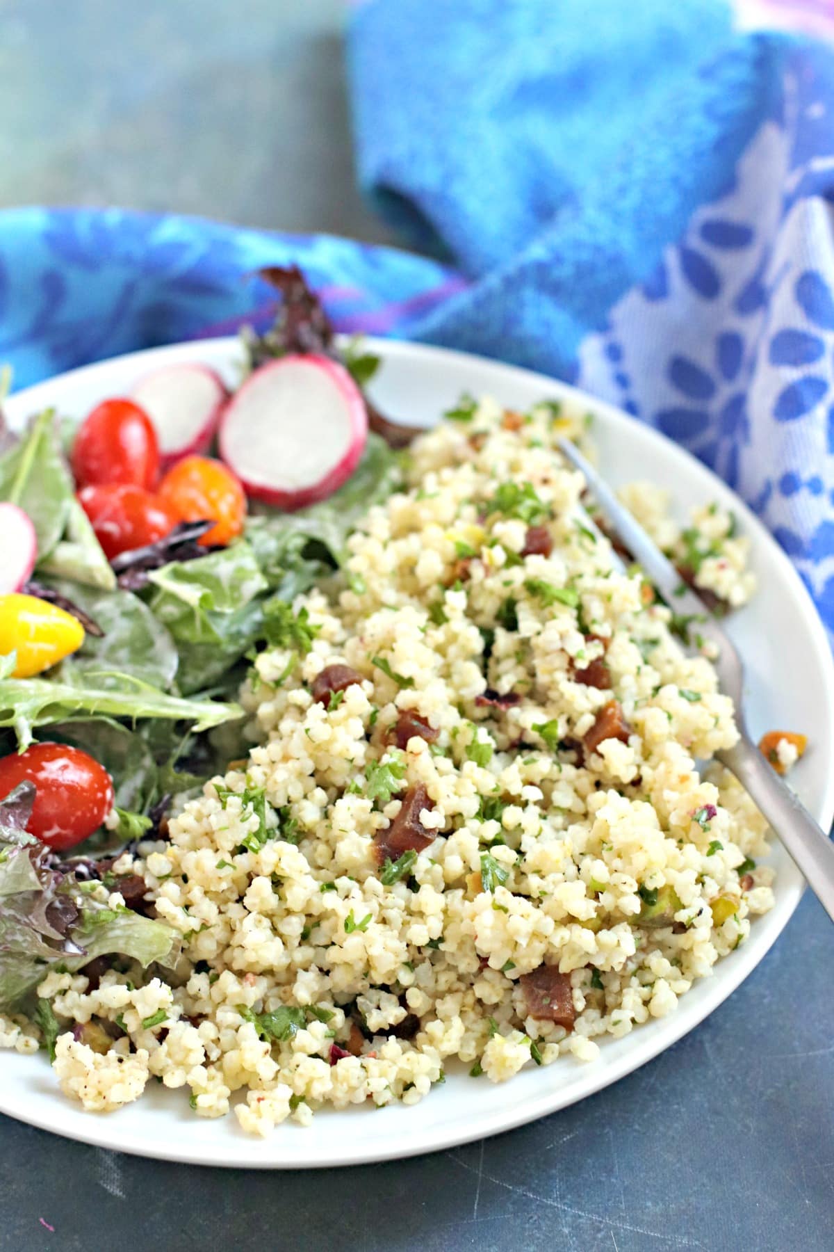 White plate with Mediterranean millet pilaf with a fork in it and a mixed green salad on the side