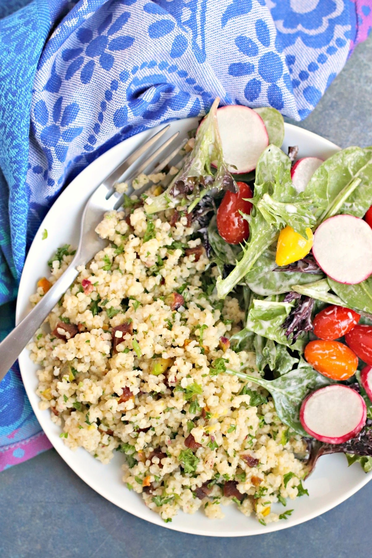 Plate with millet pilaf with fork and a mixed green salad next to a blue napkin.