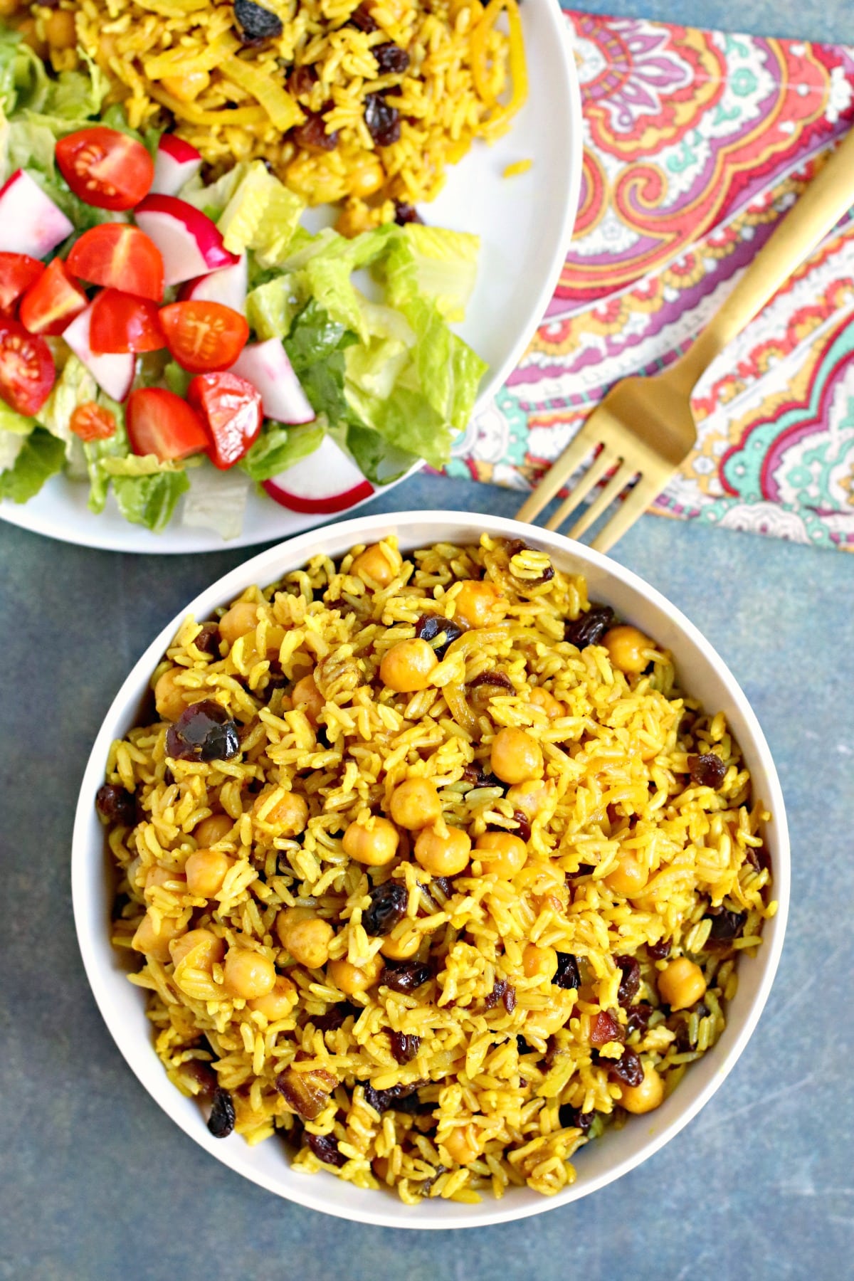 Overhead of bowl of basmati rice pilaf and a plate of salad and rice with a gold fork.