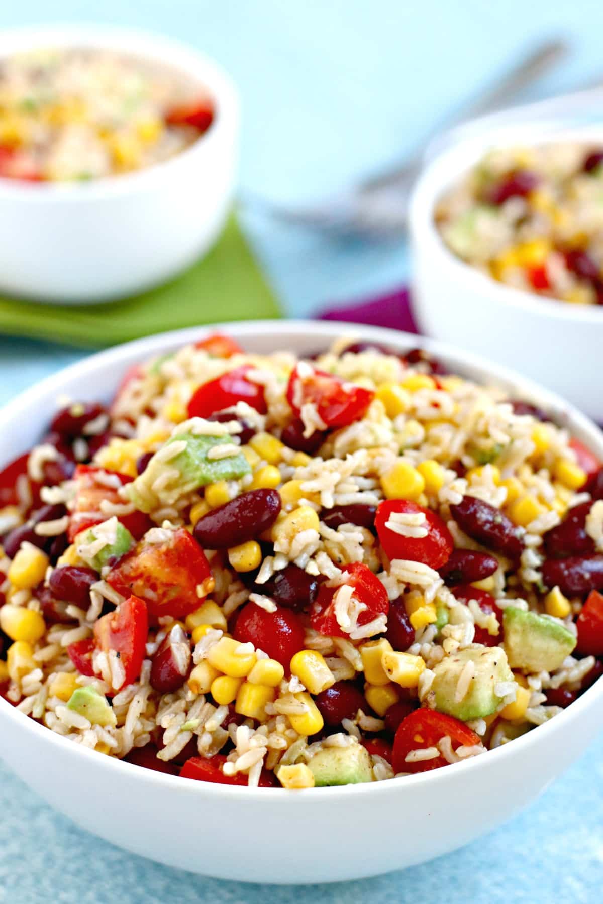Close up of bowl of Southwestern brown rice salad with corn, kidney beans, tomatoes, and avocado.
