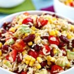 Bowl of brown rice salad with beans, corn, tomatoes, and avocado, with text overlay: Brown Rice Salad with Beans and Corn.
