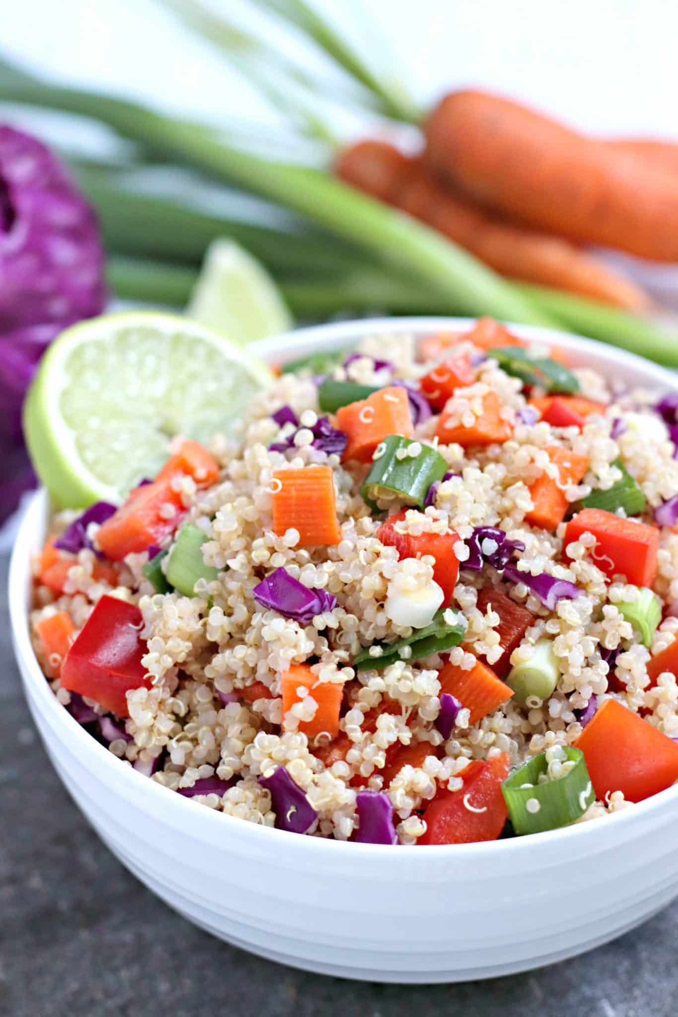 Close up of bowl of vegan quinoa salad with carrots, green onions, and red cabbage in the background.