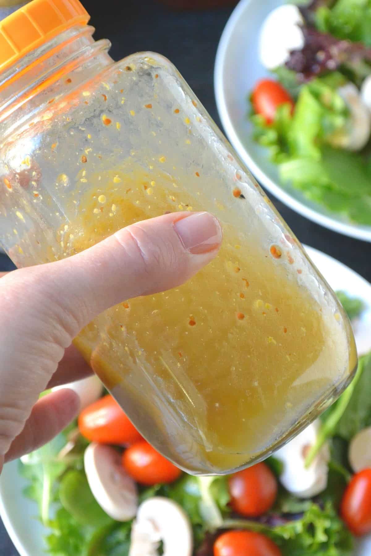 Close up of hand shaking bottle of salad dressing above plates of salad