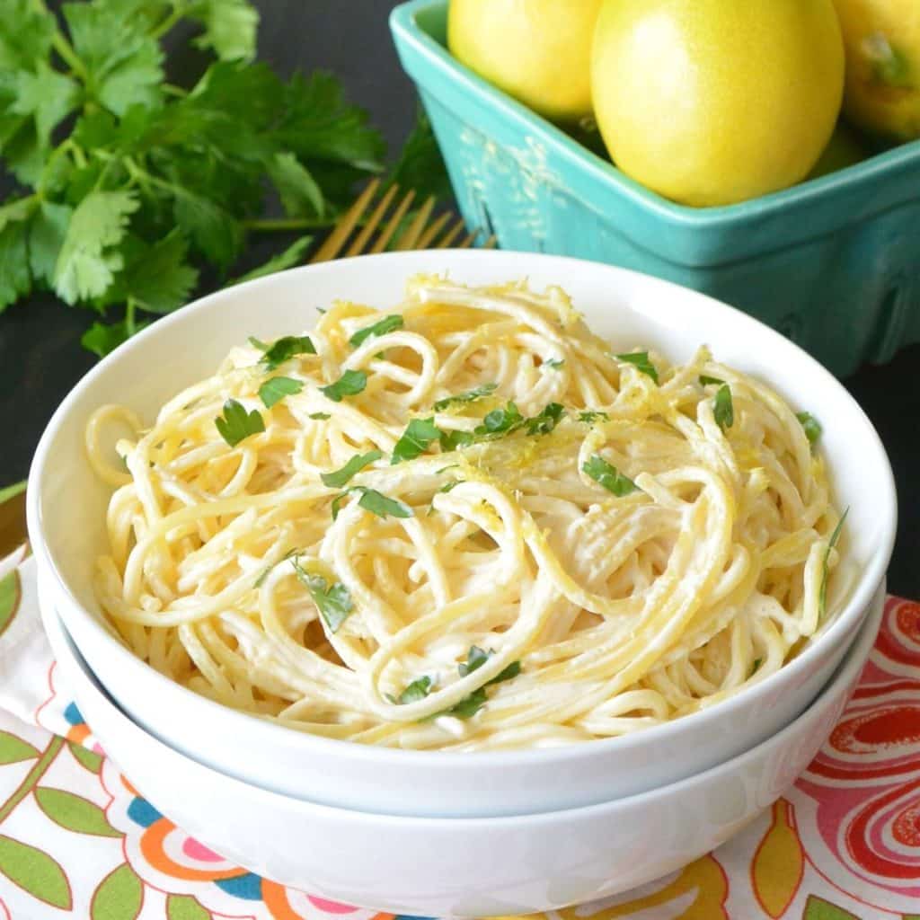 White bowl containing Lemon Dairy Free Pasta Sauce with aqua basket of lemons and parsley in the background