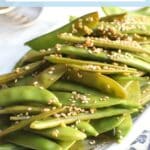 Platter of sauteed sugar snap peas garnished with sesame seeds, with text overlay: Sauteed Sugar Snap Peas with Garlic and Tamari.