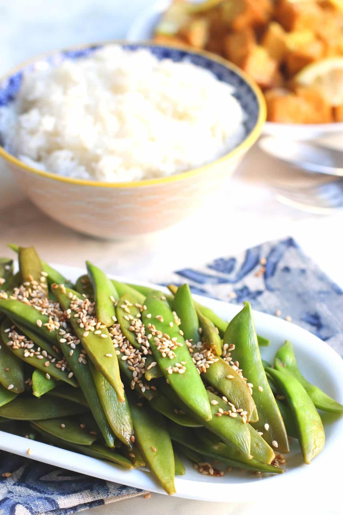 Platter of peas with a bowl of rice and platter of lemon tofu in the background