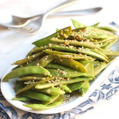 Platter of sugar snap peas topped with toasted sesame seeds.