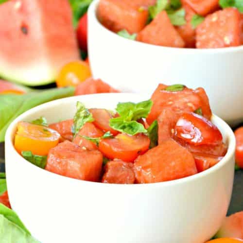 Watermelon salad in white bowls with wedge of watermelon in the background