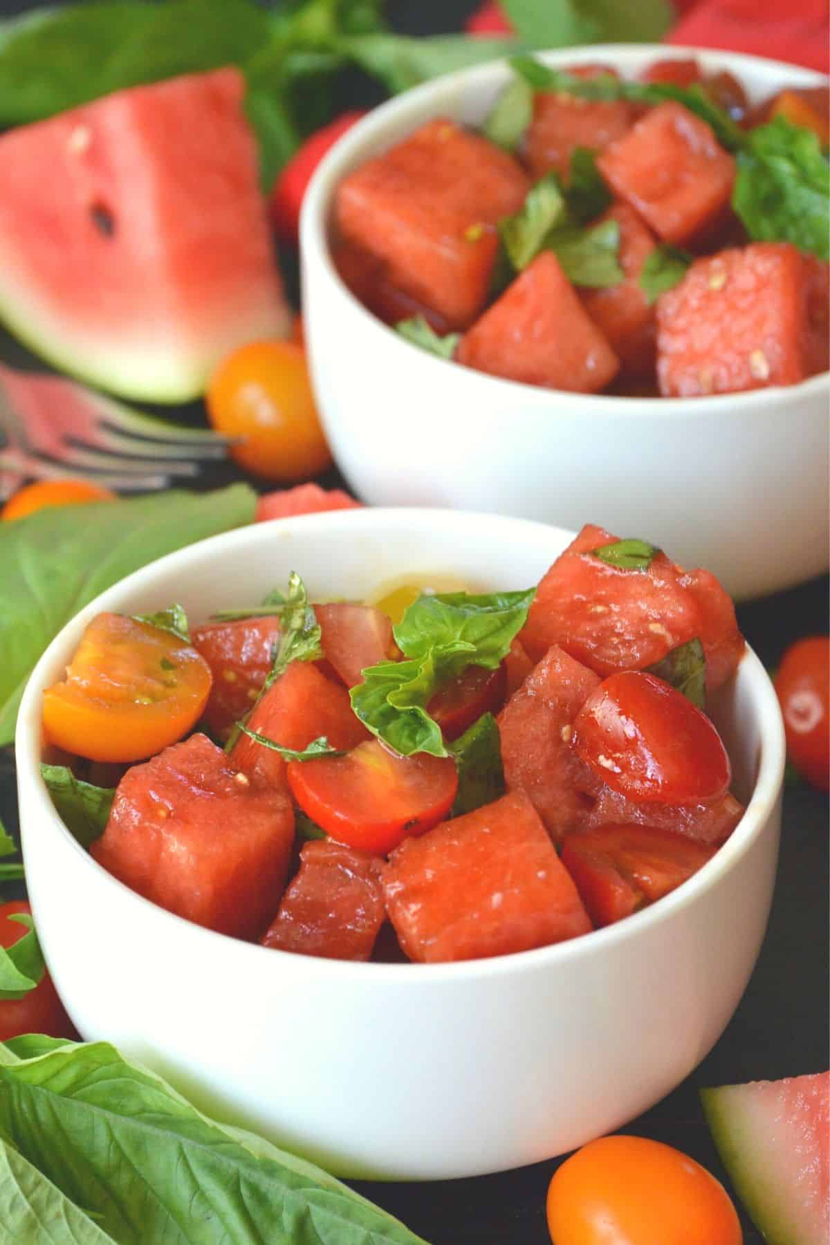 Bowls of Watermelon Tomato Salad garnished with fresh basil with a wedge of melon in the background