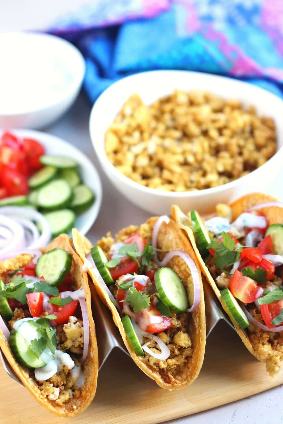 Tofu tacos on a platter with bowl of filling, vegetables toppings, and sauce in the background