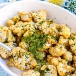 Casserole dish with roasted cauliflower garnished with fresh dill.