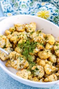 Casserole dish with roasted cauliflower garnished with fresh dill.