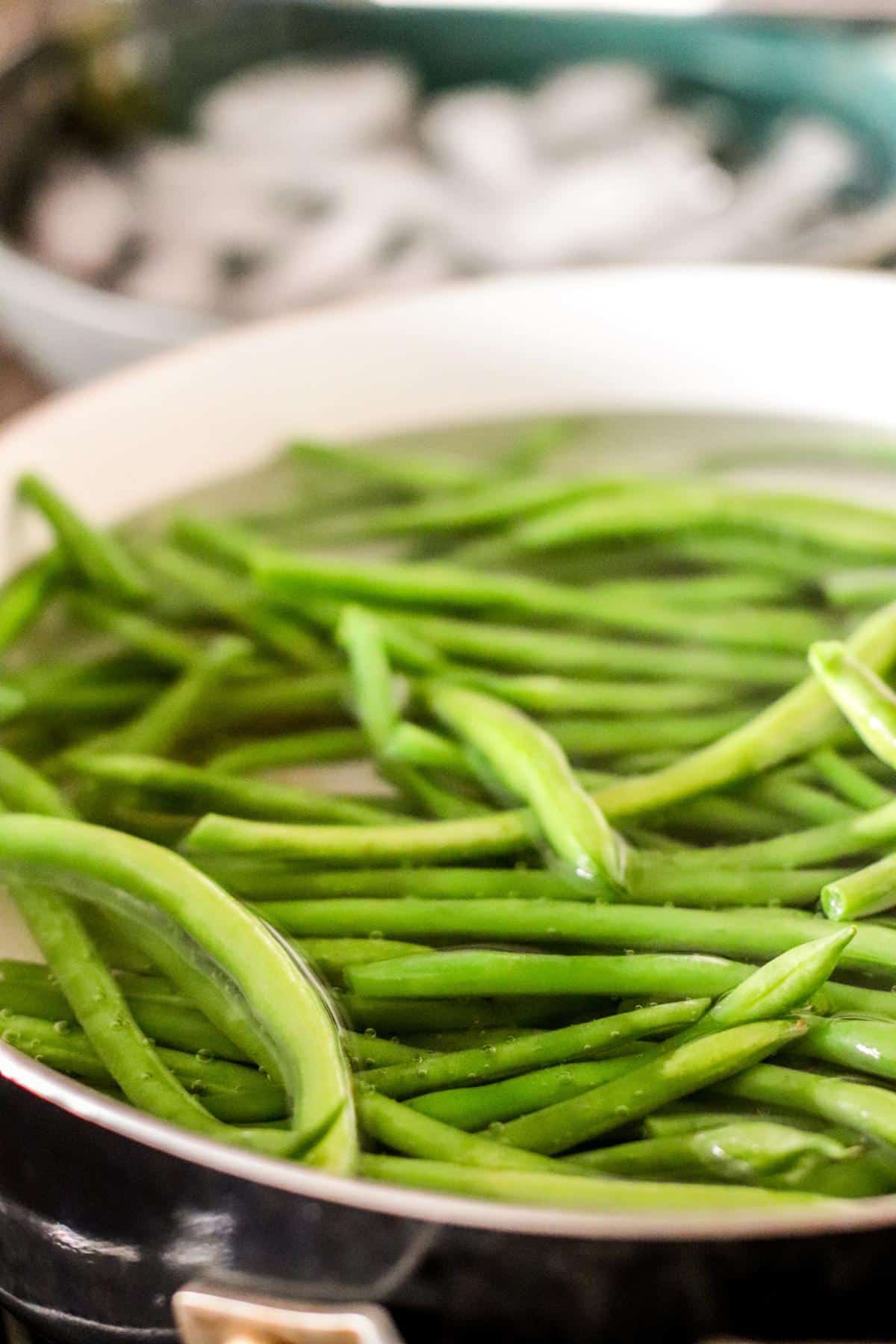 Quickly cooking the green beans in a pot of boiling water with an ice bath ready to go in the background.