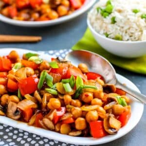 Platte of chickpea stir fry with bowl of rice behind it.