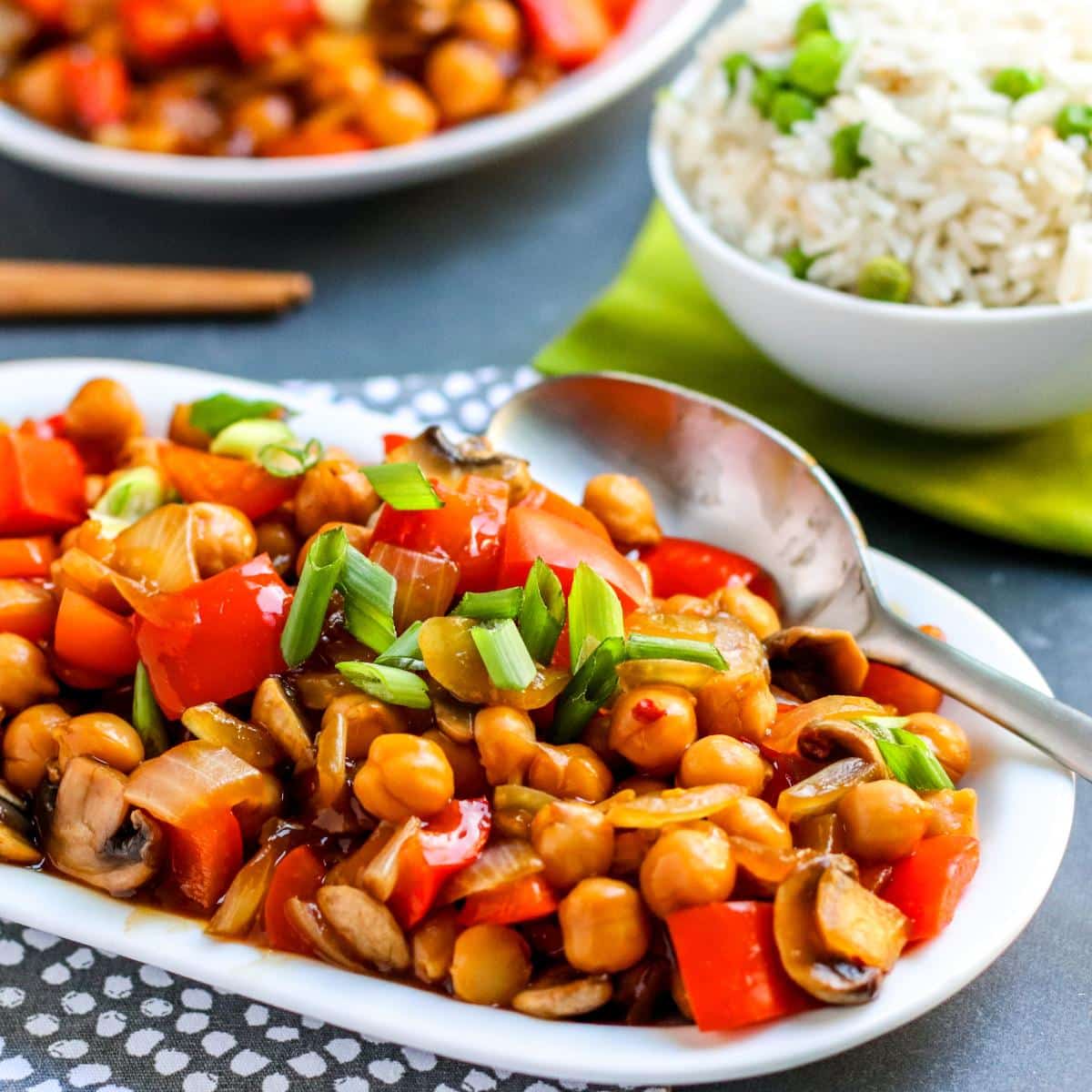 Platte of chickpea stir fry with bowl of rice behind it.