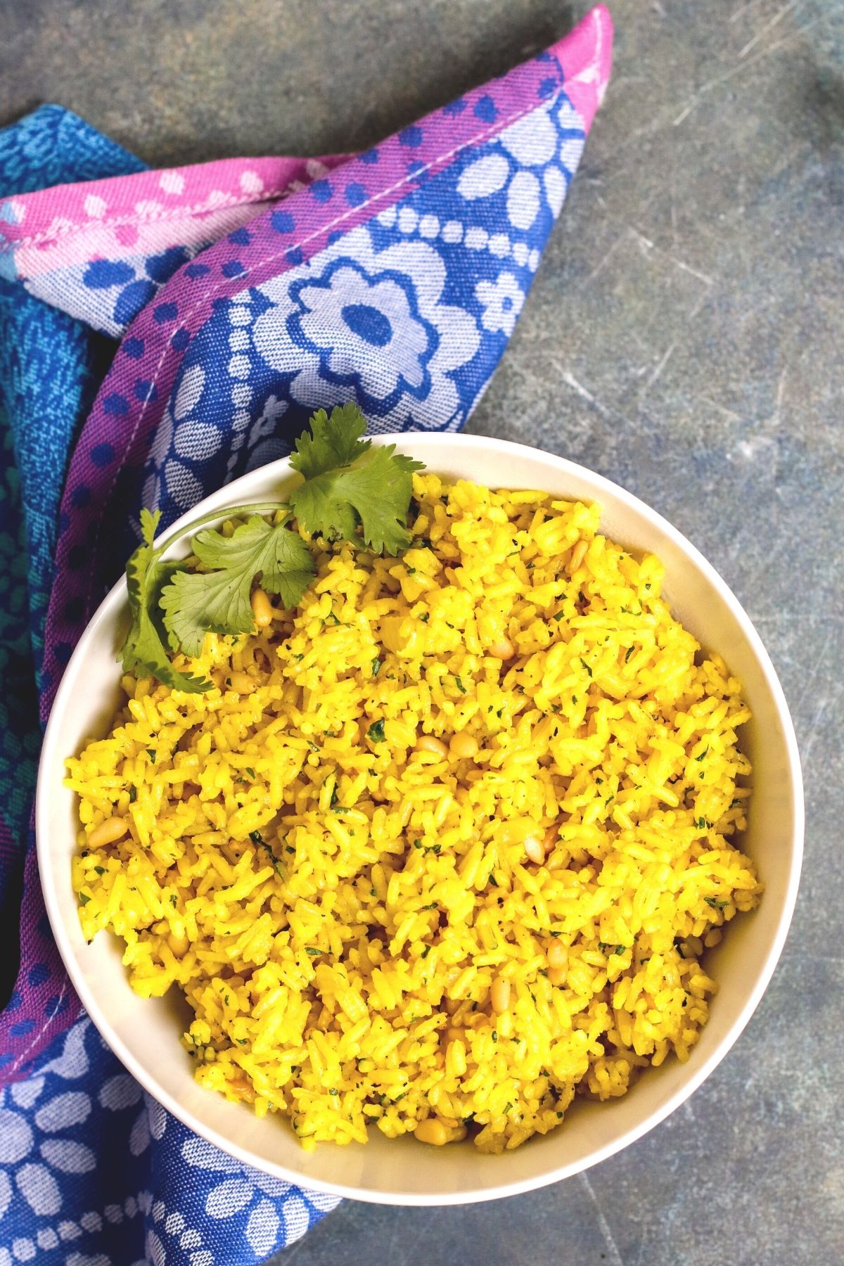 Overhead of bowl of turmeric rice and blue floral napkin.