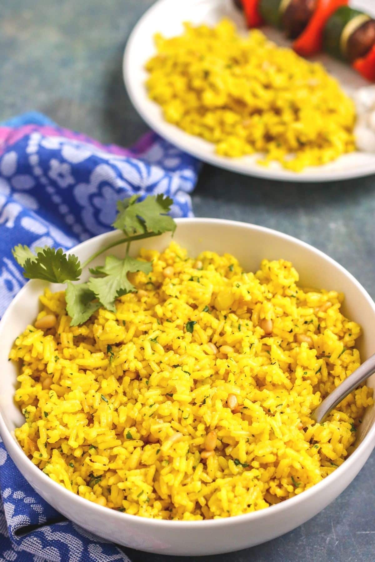 Serving bowl of yellow rice with dinner plate in the background.