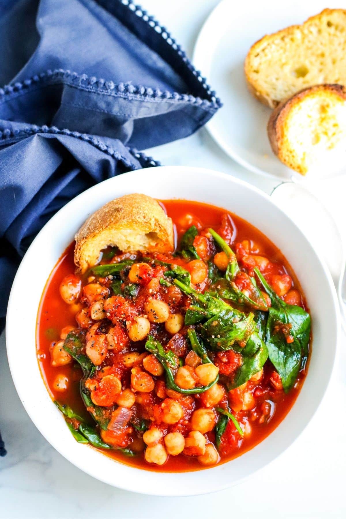 Overhead of a bowl of soup with a piece of bread on the side and a blue napkin.