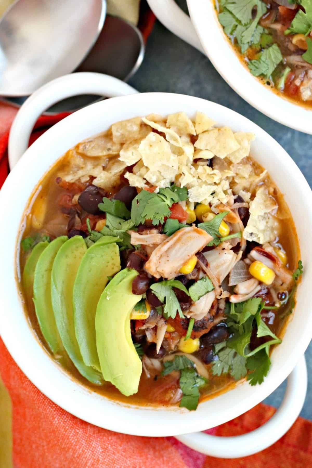 Close up of bowl of taco soup topped with avocado slices, fresh cilantro, and broken tortilla chips