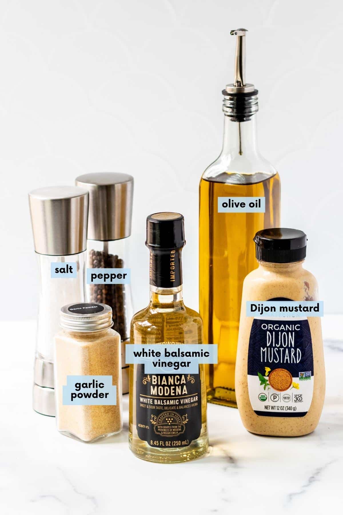 Bottles of olive oil, white balsamic vinegar, and Dijon mustard, and salt, pepper, and garlic powder.